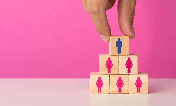Building blocks representing women are placed in a pyramid shape with a block representing a man at the top.