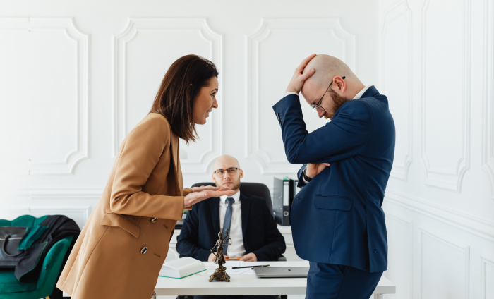 A man and woman engaged in a disagreement with a boss sat behind them. 